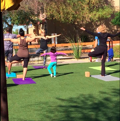 Adults and a child practicing yoga on the Postino East lawn