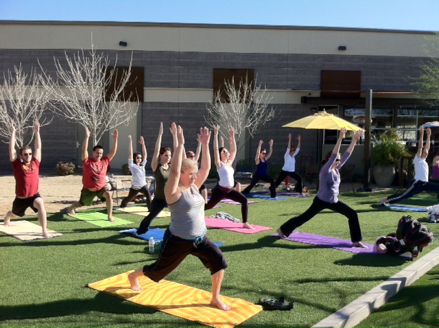 A group raising their arms in warrior pose outside Postino East