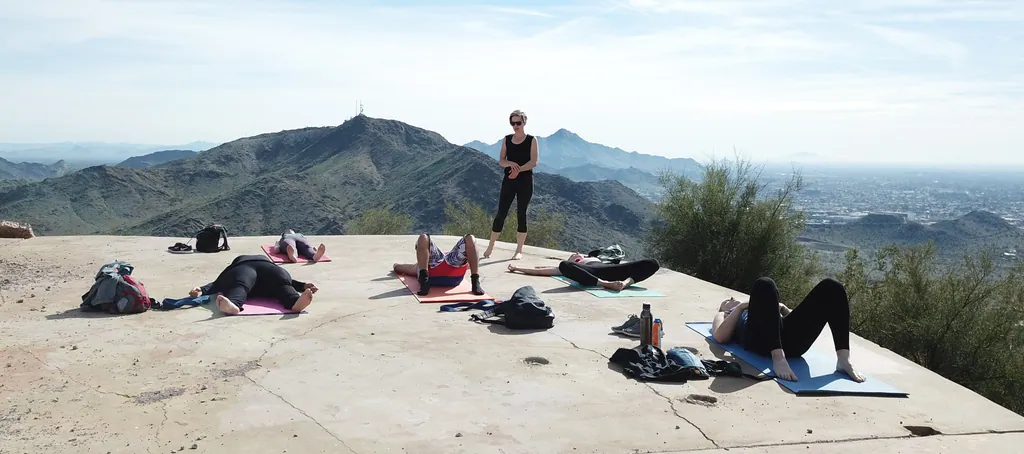 A yoga instructor and participants practicing together on a mountain overlook