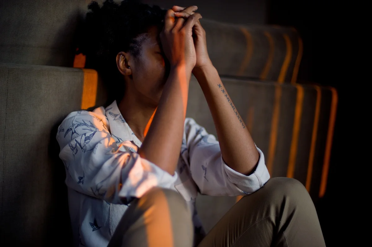 A woman seated with her hands clasped against her forehead